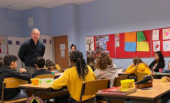 Imagem de uma sala de aula com um professor na frente e cheio de alunos