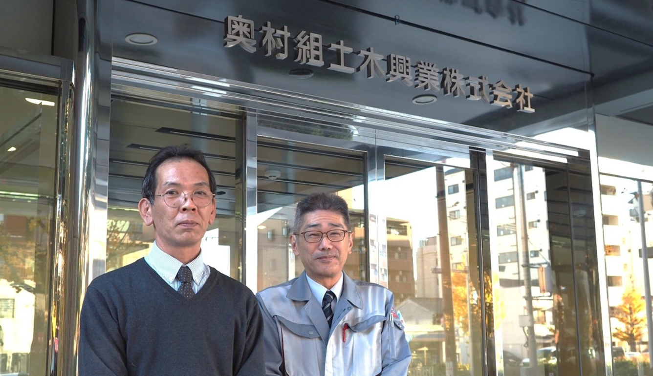 写真：奥村組土木興業株式会社 経営本部 情報システム室 室長 桑名 良宜（くわな・よしたか）氏（右）と同本部 情報システム室 情報システム課 課長 髙田 亮（たかだ・りょう）氏（左）。